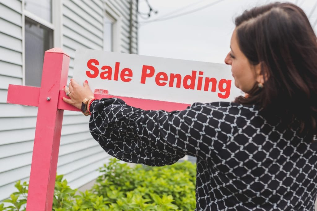 woman posting a sale pending sign in front of a house